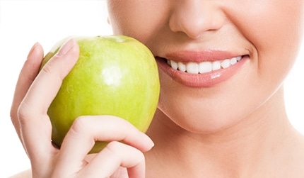 A smiling woman holding a green apple.